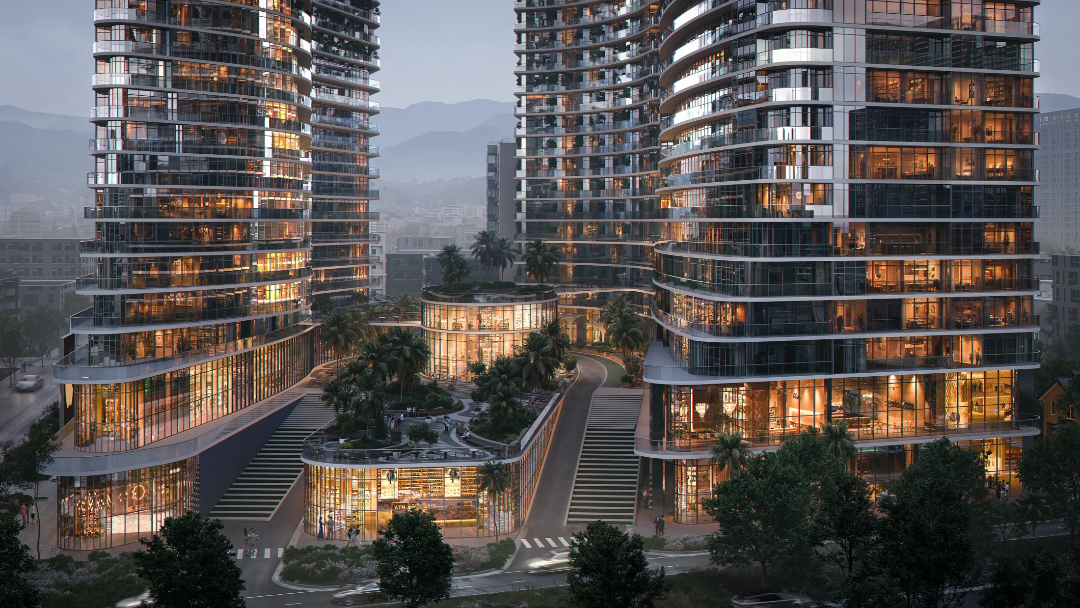 OPUS Signature at dusk — the lit street-level retail and the two towers against the Caucasus foothills